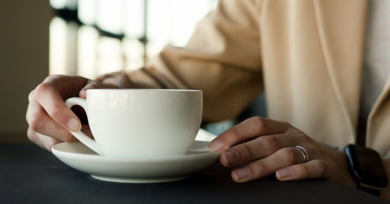 Woman holding a white coffee cup on a saucer at a table